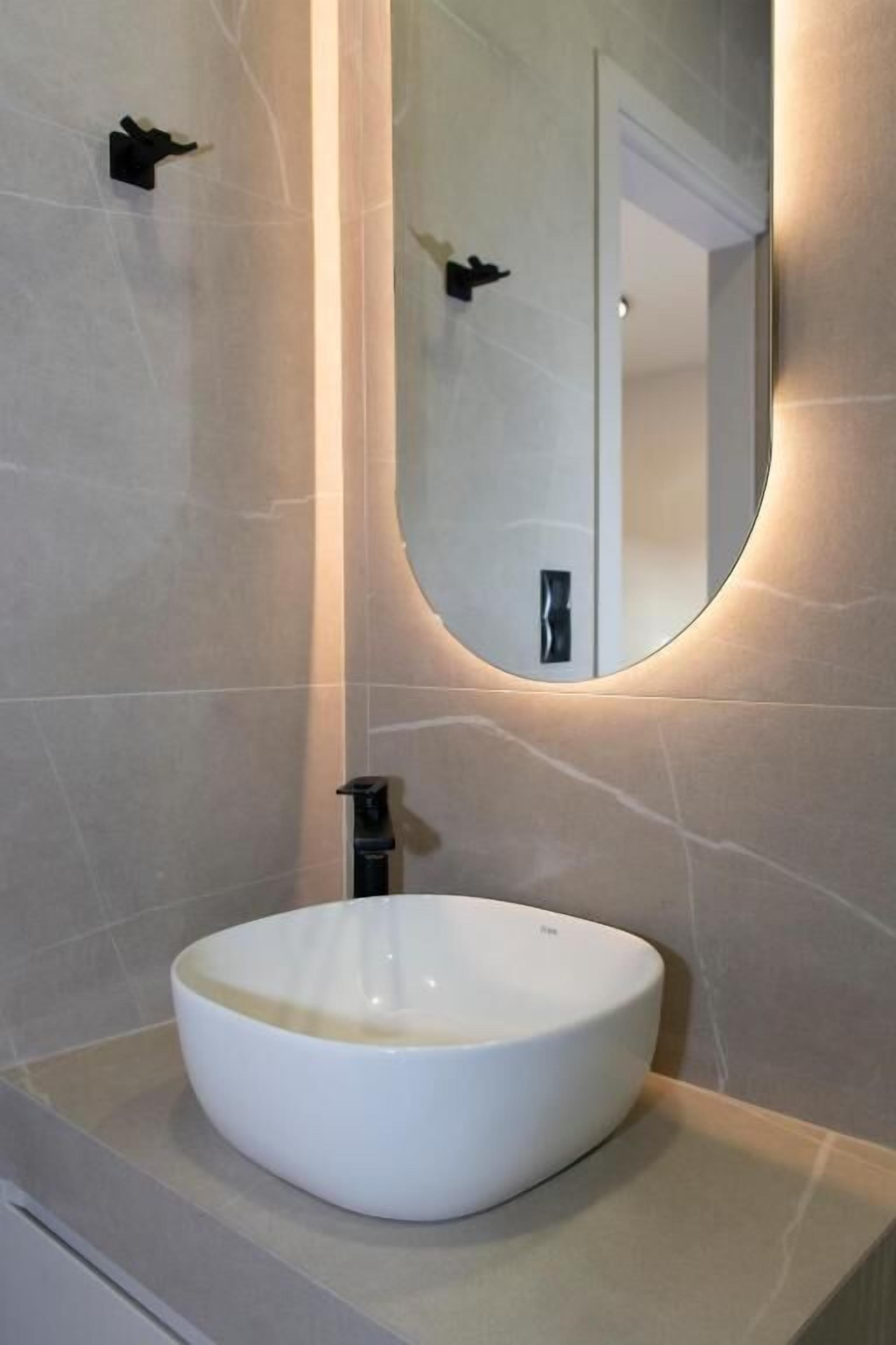 A bathroom with a white vessel sink, a round mirror, and a modern faucet.