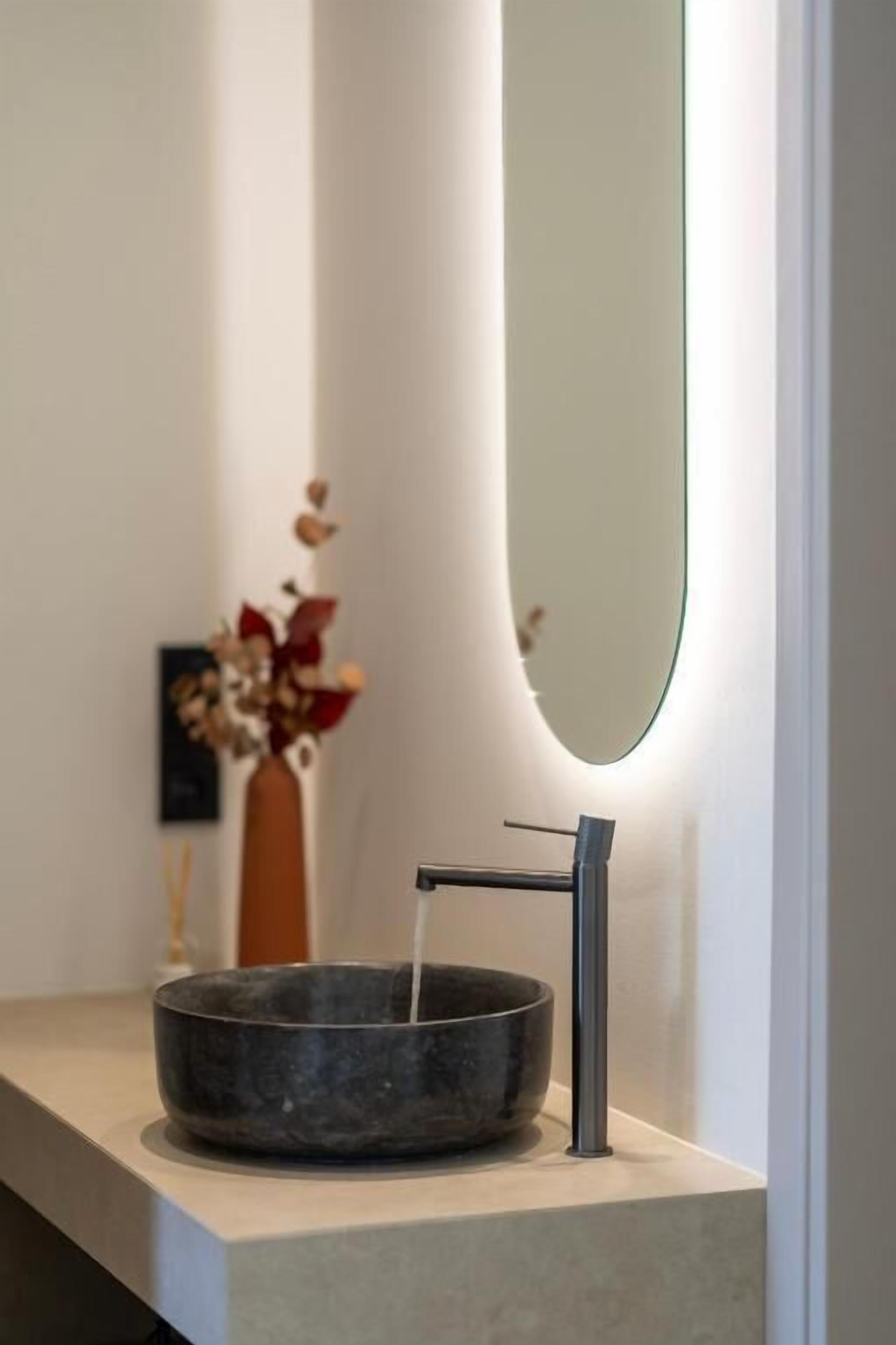 Ett modernt badrum med en minimalistisk design, med en rund tvättställ, en stilren blandare och en stor spegel.