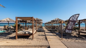 Una playa con pasarelas de madera, sombrillas de techo de paja y sillas de descanso.