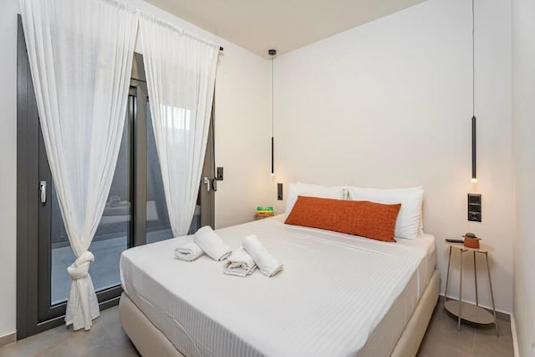 A hotel room with a bed, white curtains, a small table with a plant, and a wall-mounted light fixture. - Lotus Serenity Suites (Malevizi)
