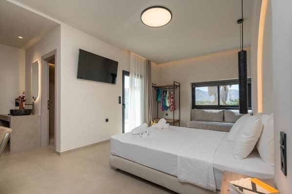 A modern bedroom with a large bed, a TV mounted on the wall, and a window with a view. - Lotus Serenity Suites (Malevizi)