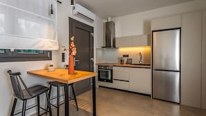 Una cocina moderna con una mesa de madera, dos taburetes negros, un refrigerador de acero inoxidable y un horno empotrado.