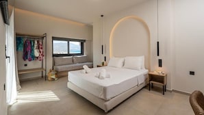 Un dormitorio moderno con una cama grande, un banco con toallas de colores, una mesita de noche y vistas a las montañas a través de una ventana.