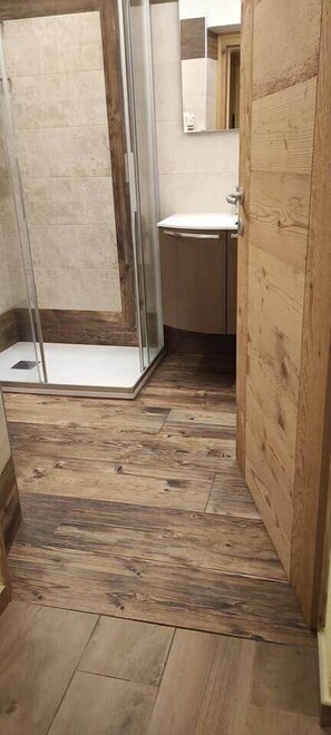 Ein Badezimmer mit Holzboden, einer Duschkabine aus Glas und einer Holztür.
