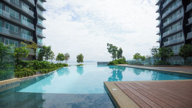 A swimming pool with a wooden deck, surrounded by greenery and modern buildings. - QuayWest (George Town)