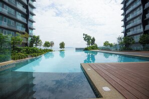 A swimming pool with a wooden deck, surrounded by greenery and modern buildings. - QuayWest (George Town)