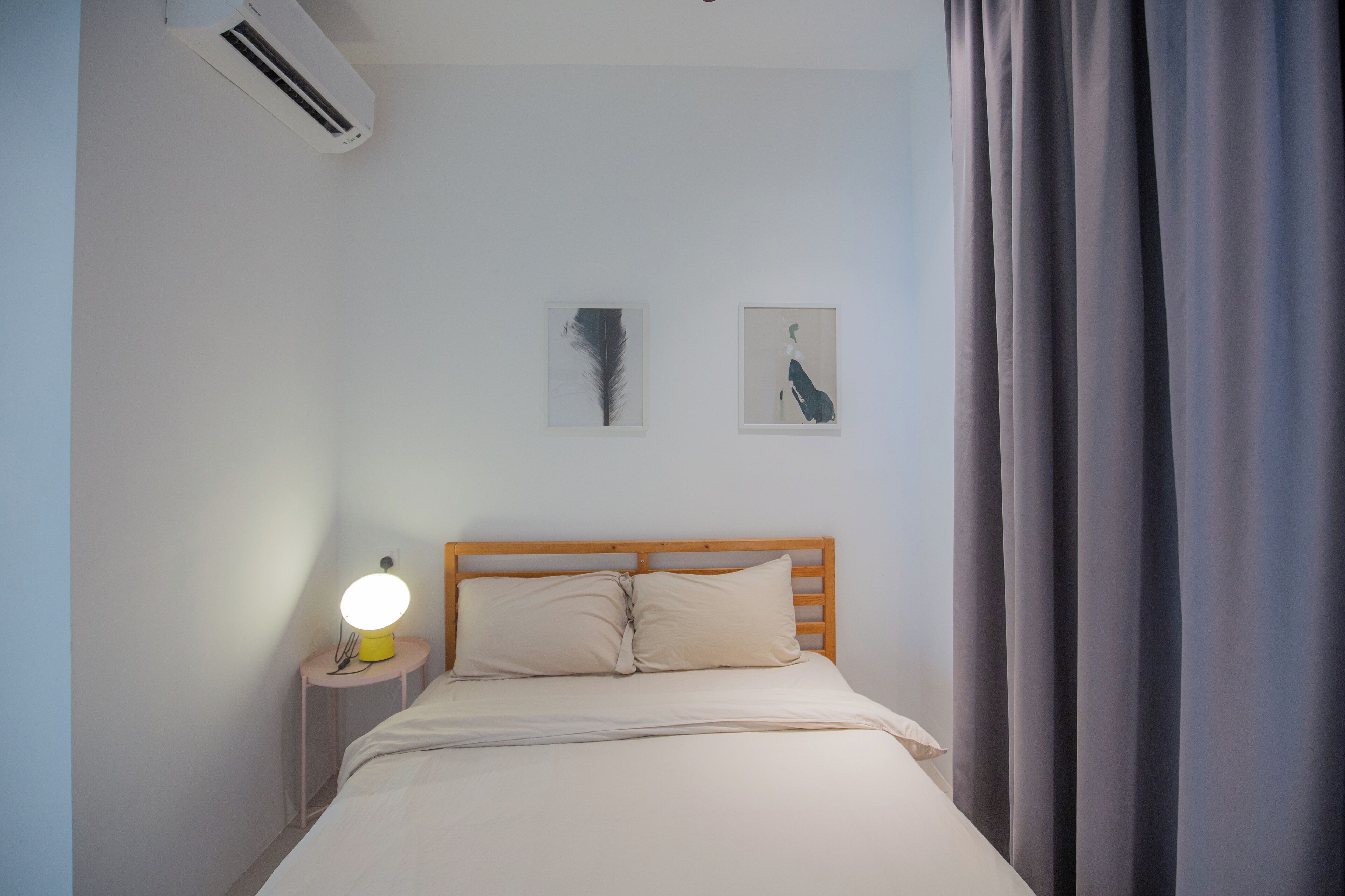 A bedroom with a bed, a nightstand with a lamp, and two wall-mounted pictures.