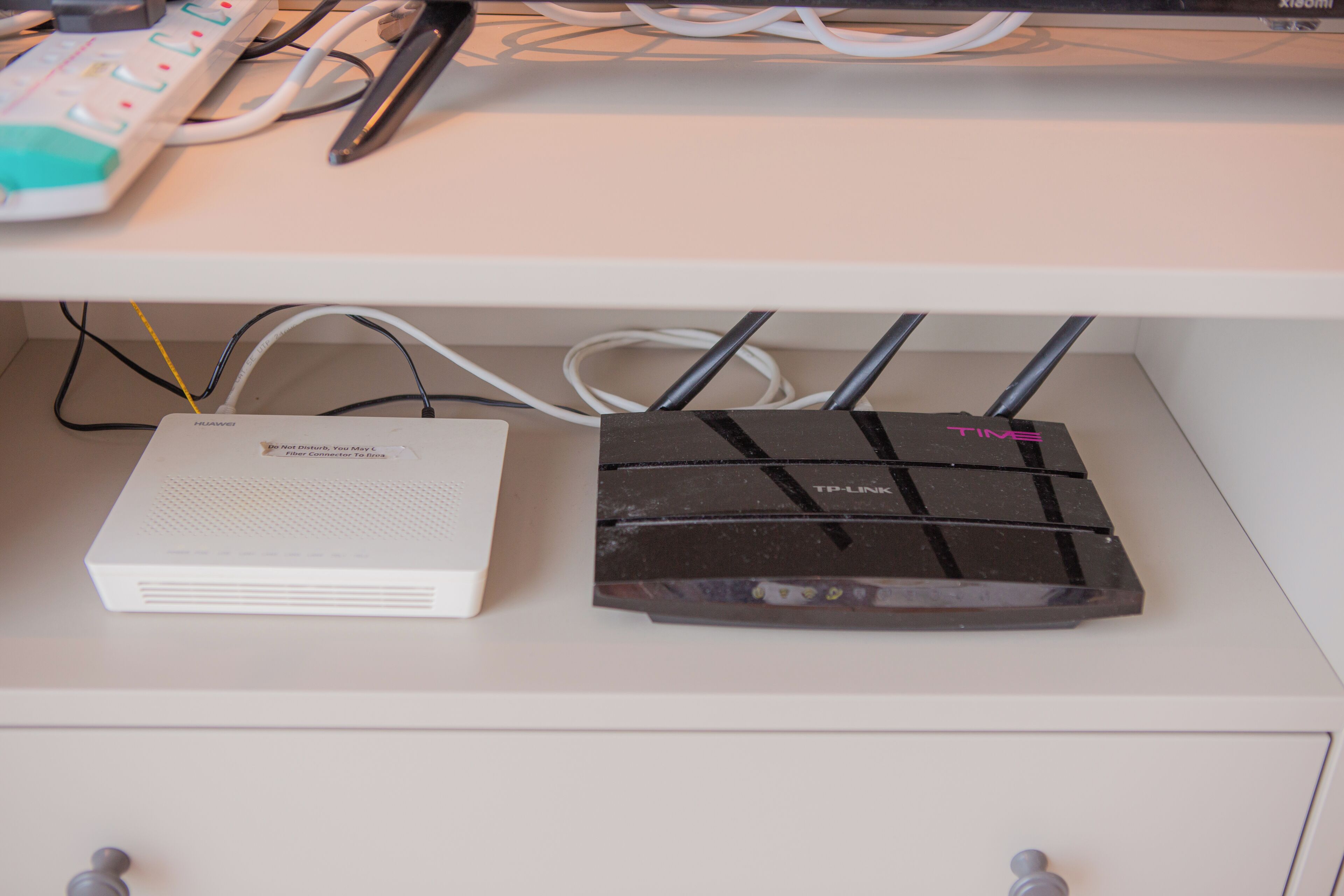 A white desk with a white router and a black TP-Link router connected to it.
