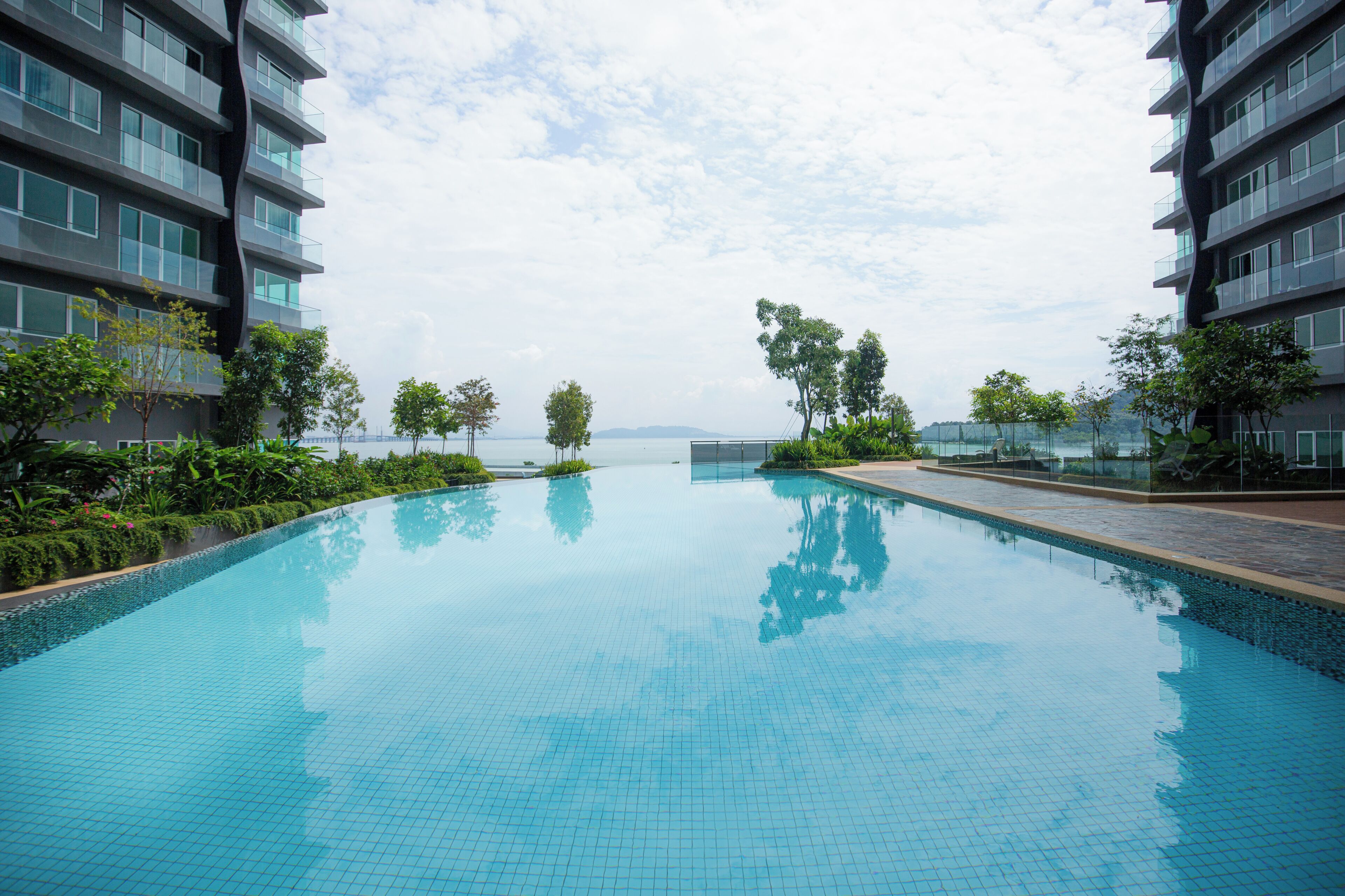 Piscina con vistas claras al mar, rodeada de edificios modernos y vegetación.