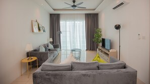 A modern living room with a grey sofa, a small round table, a television, and a ceiling fan. - QuayWest (George Town)