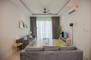 Una sala de estar moderna con un sofá gris, una mesita redonda pequeña, un televisor y un ventilador de techo.