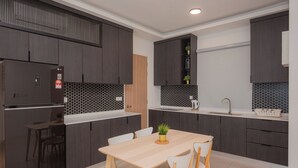 A modern kitchen with dark cabinets, a wooden table, and white chairs. - QuayWest (George Town)