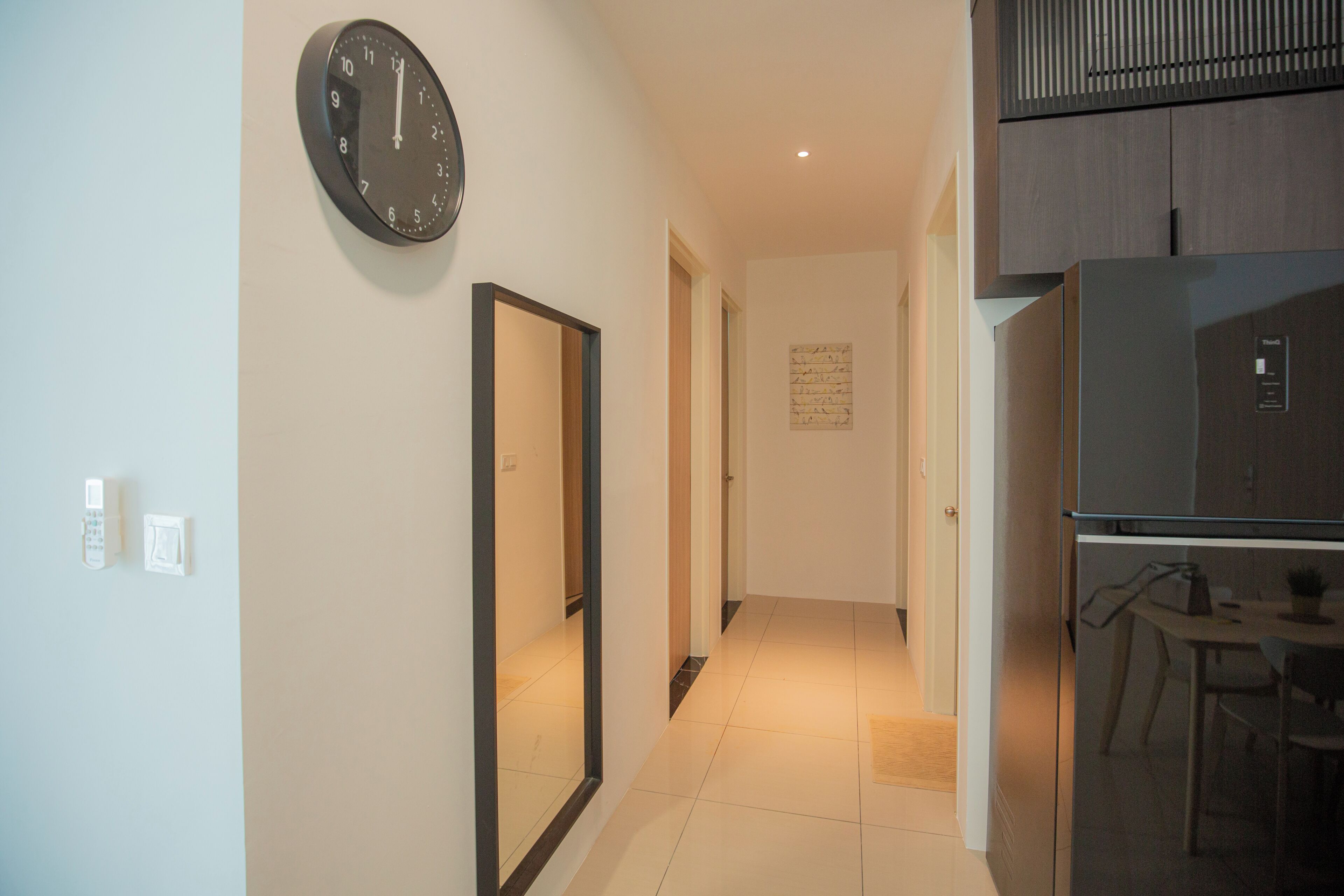 A hallway with a clock, a refrigerator, and a dining area.