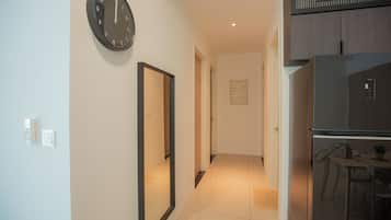 A hallway with a clock, a refrigerator, and a dining area.