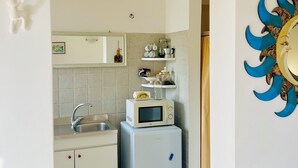 Une cuisine de taille réduite, avec un micro-ondes posé sur le dessus d’un réfrigérateur, un évier et une étagère contenant des ustensiles de cuisine.