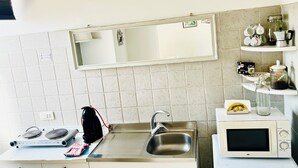Une petite cuisine équipée d’un évier, d’une cuisinière, d’un four à micro-ondes et d’une étagère contenant des ustensiles de cuisine.