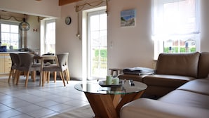 Ein Wohnzimmer mit Glastisch, einer Couch und einem Essbereich mit Stühlen.
