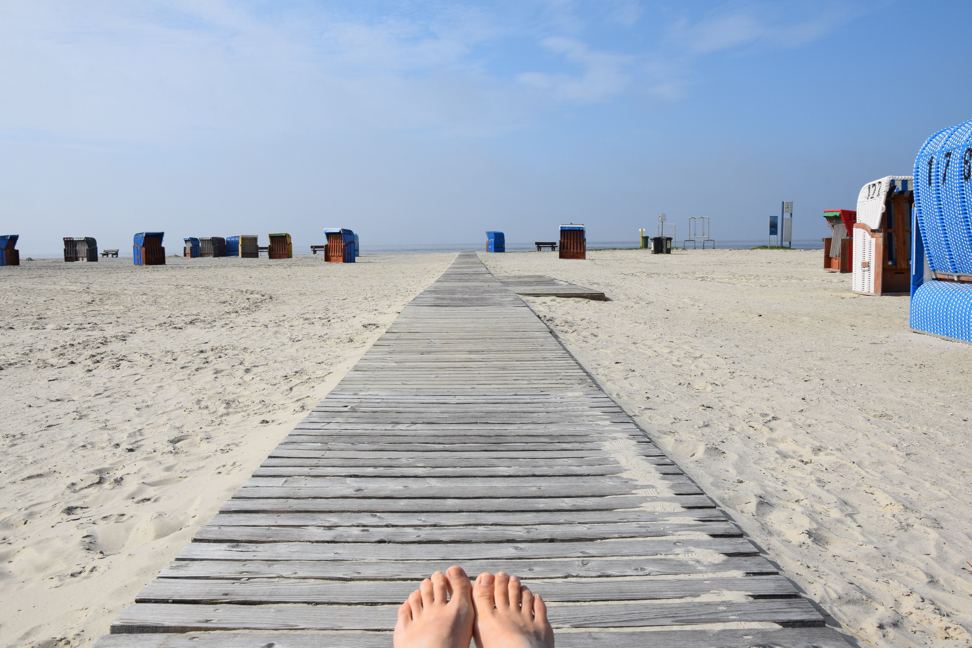 Een houten looppad dat naar strandhutten op een zandstrand leidt.