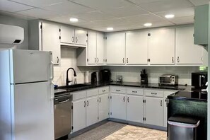 Una cocina moderna con armarios blancos, un refrigerador de acero inoxidable, una cafetera y un cubo de basura.
