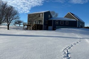 Una casa de dos pisos con un garaje grande, rodeada de nieve y un cielo despejado.
