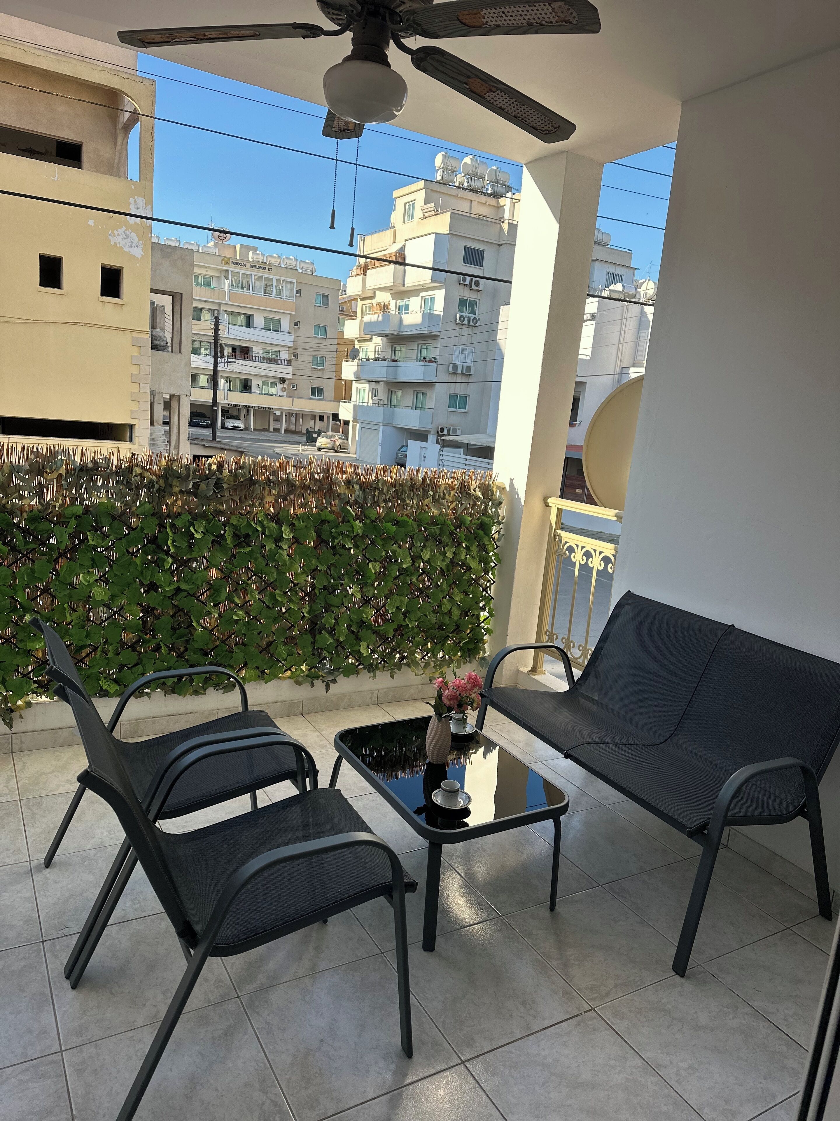 A balcony with two black chairs, a small table, and a ceiling fan.