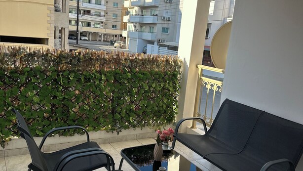 Ein Balkon mit zwei schwarzen Stühlen, einem kleinen Tisch und einem Deckenventilator.