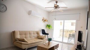 Ein Wohnzimmer mit einem beigefarbenen Sofa, einem Holztisch, einem Fernseher und einem Deckenventilator.