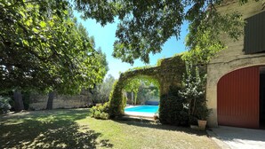 A stone archway leading to a swimming pool, surrounded by lush greenery and a stone wall. - 19th-century farmhouse combining authenticity and comfort (Gallargues-le-Montueux)