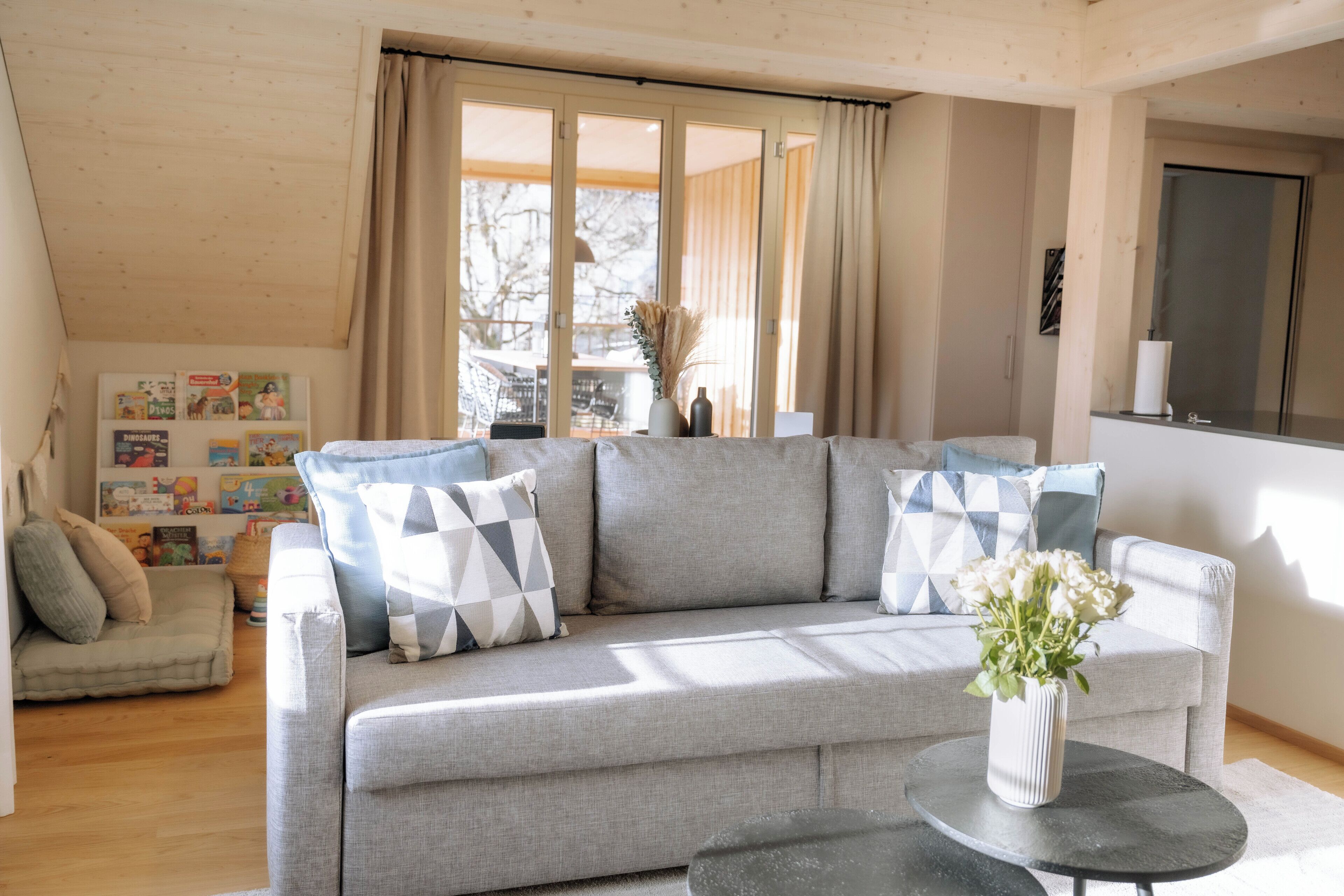 Ein modernes Wohnzimmer mit einem grauen Sofa, einem kleinen runden Tisch und einem Blumenstrauß.