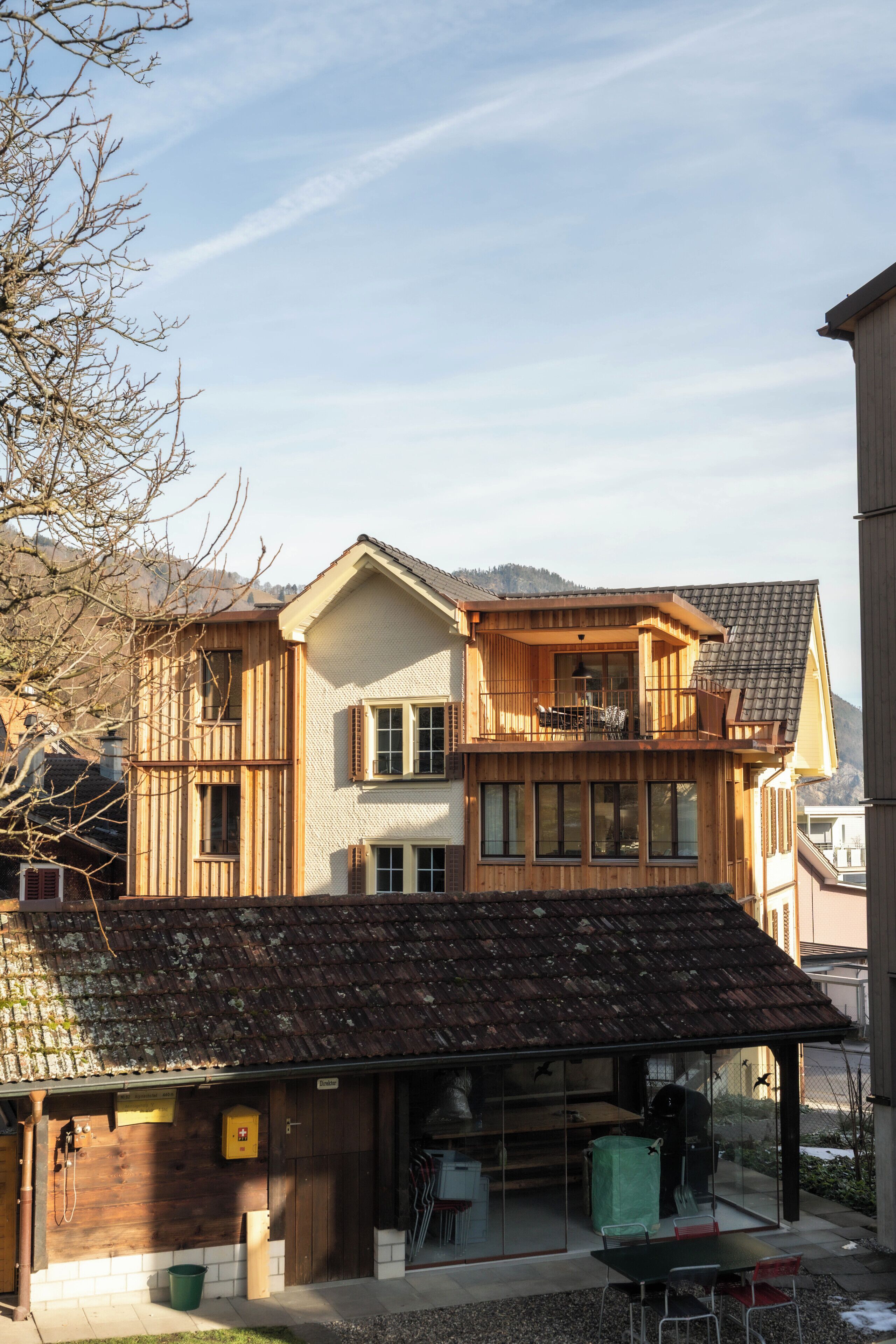 Une maison en bois à deux étages, dotée d’un balcon, d’une petite remise attenante et offrant une vue dégagée sur le paysage environnant.