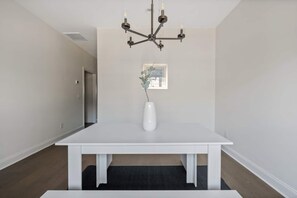 Una habitación amplia con una gran mesa blanca, una lámpara moderna y un cuadro en la pared.