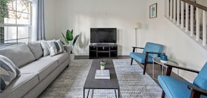 A living room with a sofa, coffee table, and chairs, a TV, and a staircase. - 1 King 2 Queens Garage Yard Washer Dryer (Old Hickory)