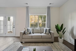 A living room with a beige sofa, a coffee table, and a potted plant. - 1 King 2 Queens Garage Yard Washer Dryer (Old Hickory)