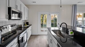 Une cuisine moderne avec des meubles blancs, des appareils en acier inoxydable et une grande fenêtre donnant sur un paysage verdoyant.