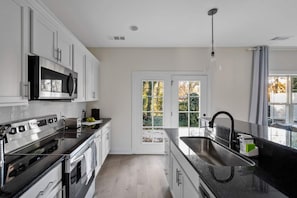 A modern kitchen with white cabinets, stainless steel appliances, and a large window with a view of greenery. - 1 King 2 Queens Garage Yard Washer Dryer (Old Hickory)