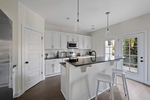 A modern kitchen with white cabinets, a central island with stools, a microwave, and a large window. - 1 King 2 Queens Garage Yard Washer Dryer (Old Hickory)