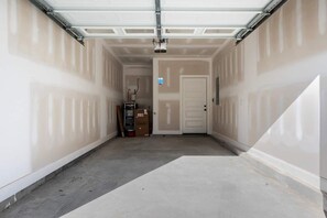 A garage with a closed garage door, a door at the end, and a concrete floor. - 1 King 2 Queens Garage Yard Washer Dryer (Old Hickory)