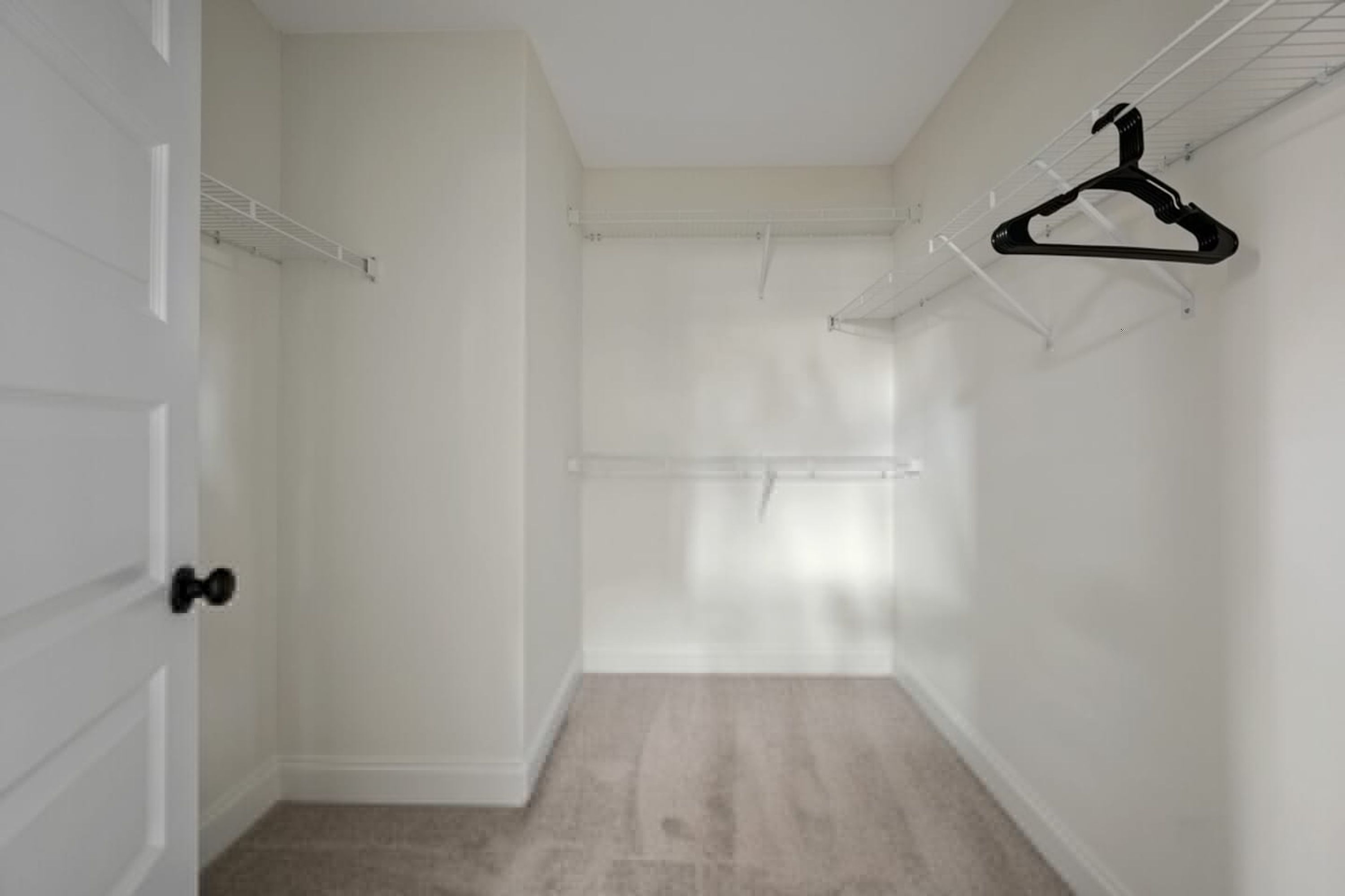 Ein begehbarer Kleiderschrank mit weißen Wänden, Holzboden und einem schwarzen Kleiderbügel an einem Drahtregal.