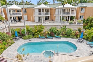 Ein Hotel mit Schwimmbad, umgeben von Liegestühlen und Sonnenschirmen, mehreren Balkonen und einem Garten.