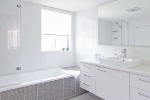 A modern bathroom with a bathtub, a sink, and a large mirror. - Macquarie Lodge Apartments (Sunshine Coast)