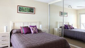 Een slaapkamer met een groot bed, een nachtkastje, een dressoir en een spiegel.