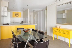 Eine moderne Küche mit einer gelben Akzentwand, einem Glastisch und einer gelben Kommode.