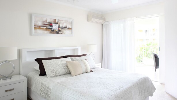 Een slaapkamer met een groot bed, een nachtkastje, een lamp en een raam met gordijnen.