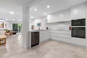 A modern kitchen with white cabinetry, a dishwasher, a microwave, and an oven. - Macquarie Lodge Apartments (Sunshine Coast)