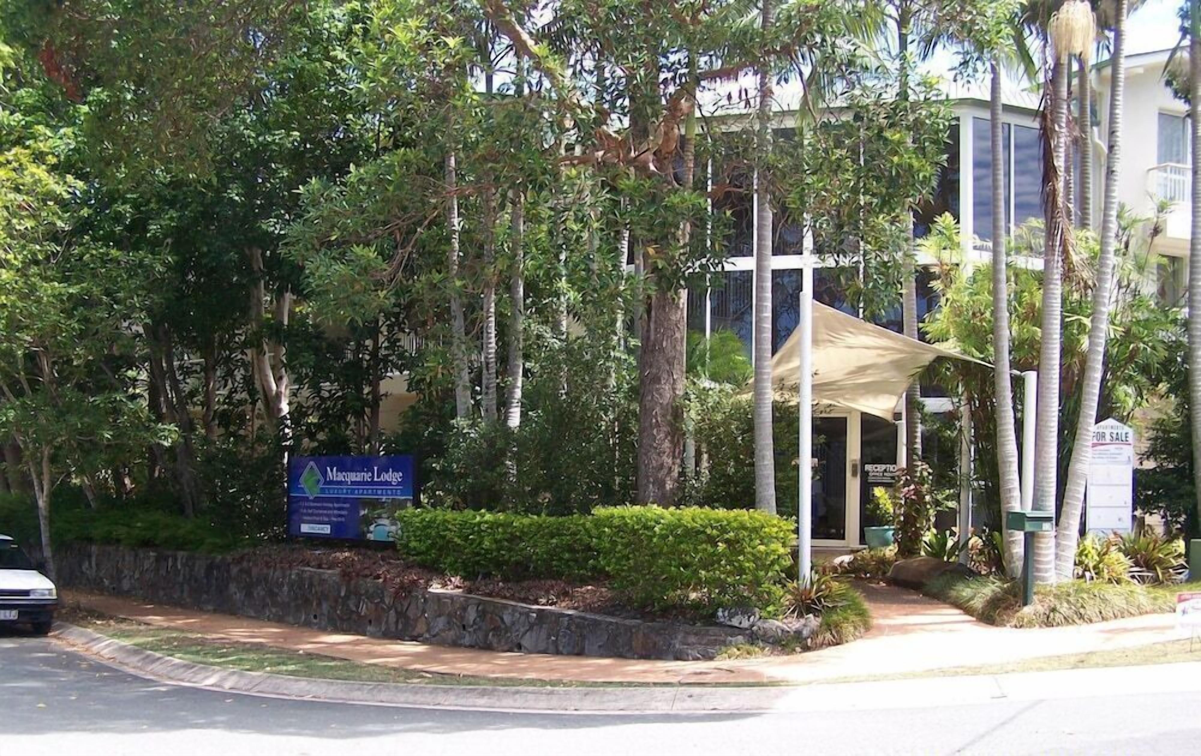 A Macquarie Lodge reception area with a sign, a covered outdoor seating area, and lush greenery.