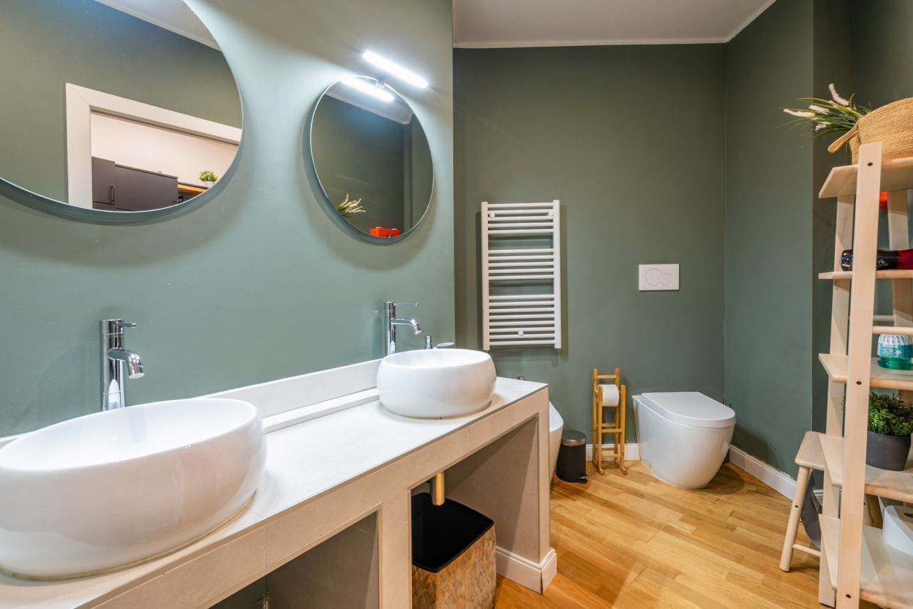 A modern bathroom with two sinks, a mirror, a towel rack, and a toilet.