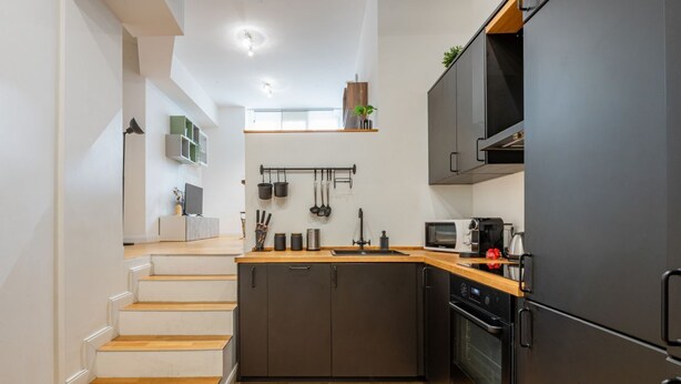 Une cuisine moderne dotée d’un îlot central, d’appareils électroménagers intégrés et d’un escalier en bois menant à un niveau supérieur.