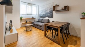Un salon moderne avec une table à manger en bois, un canapé gris et un tableau représentant un paysage urbain accroché au mur.