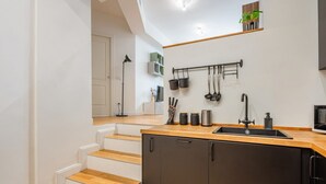 Une cuisine moderne avec des marches en bois menant à un meuble noir, un porte-ustensiles suspendu et une petite étagère ornée d’une plante.