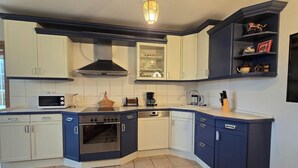 A modern kitchen with white and blue cabinetry, a built-in oven, a microwave, and a coffee maker. - Bungalow in Schlowe Am See (Borkow)